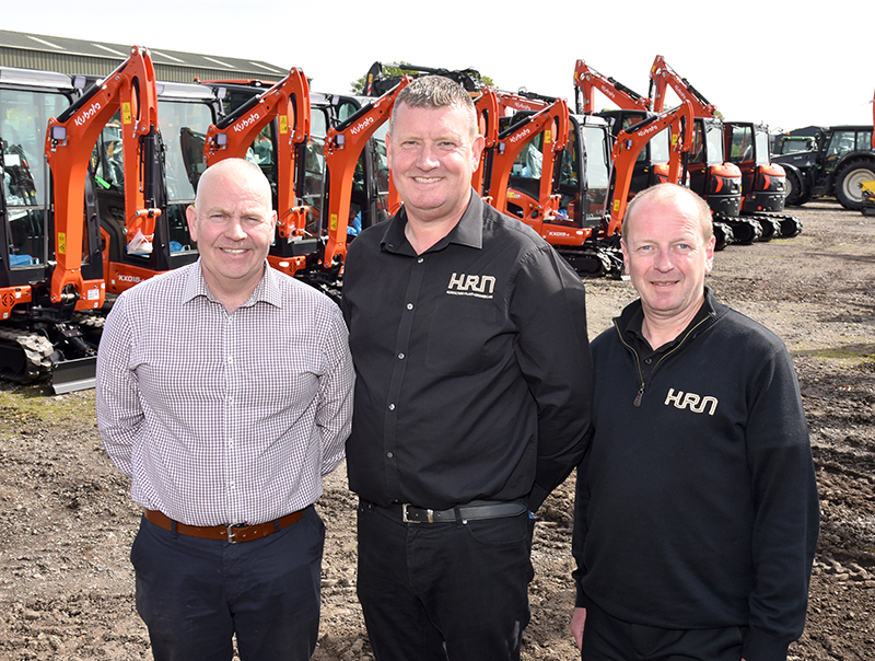 Three men standing in front of excavators