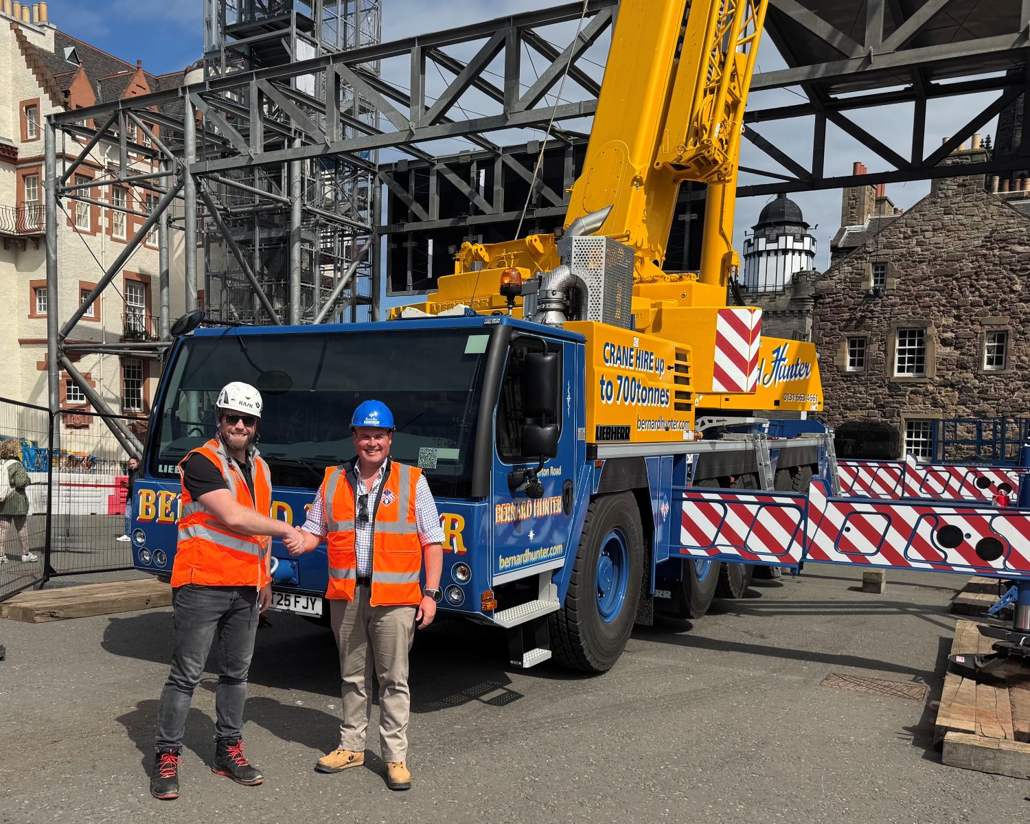 Two men shaking hands in front of crane